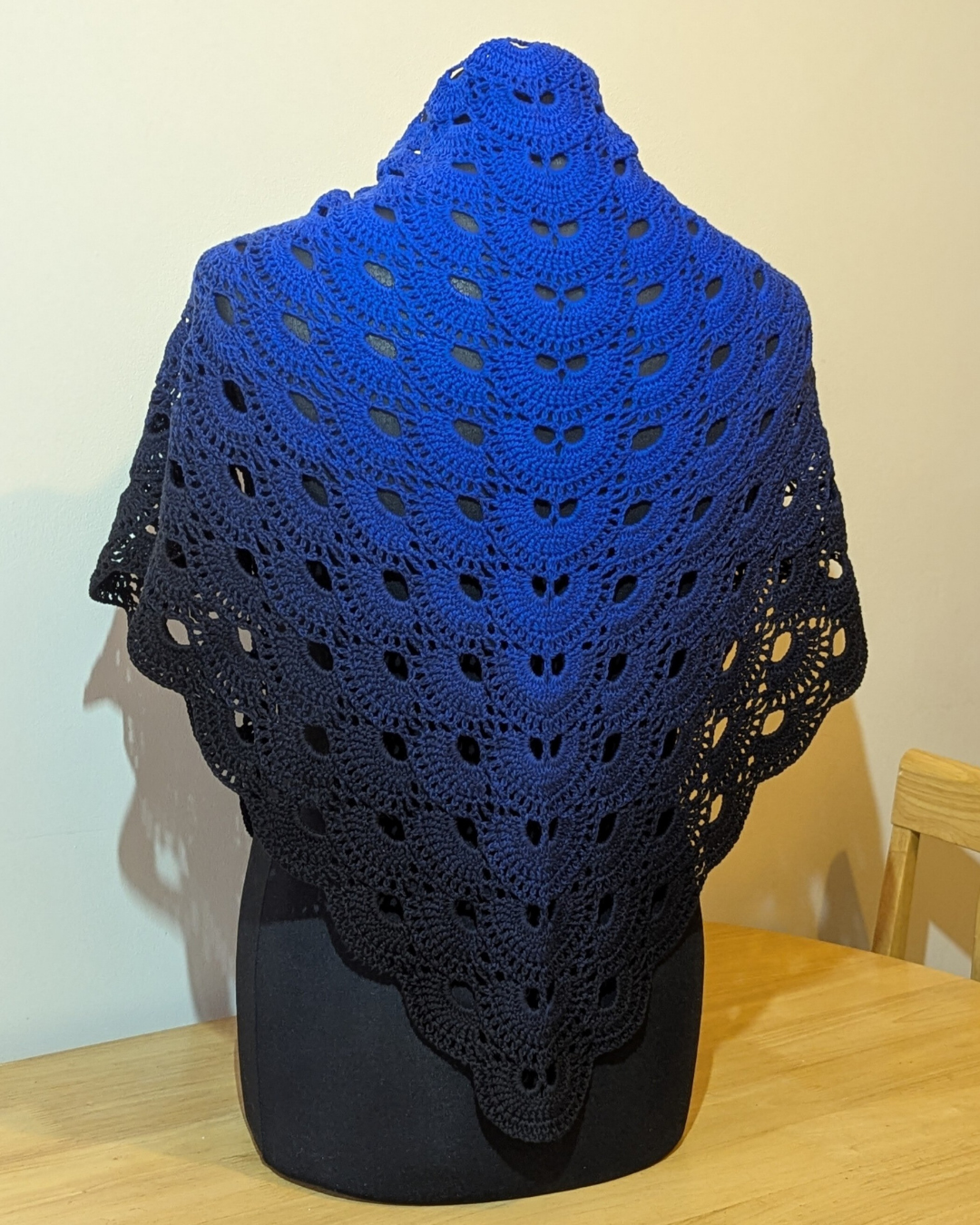 Blue crocheted shawl on a mannequin against a plain background