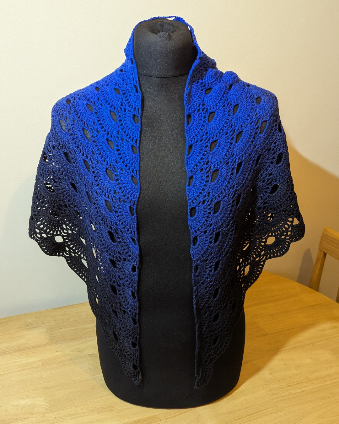 Blue crocheted shawl on a black mannequin against a plain background