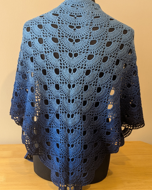 Blue crocheted shawl on a mannequin against a beige background