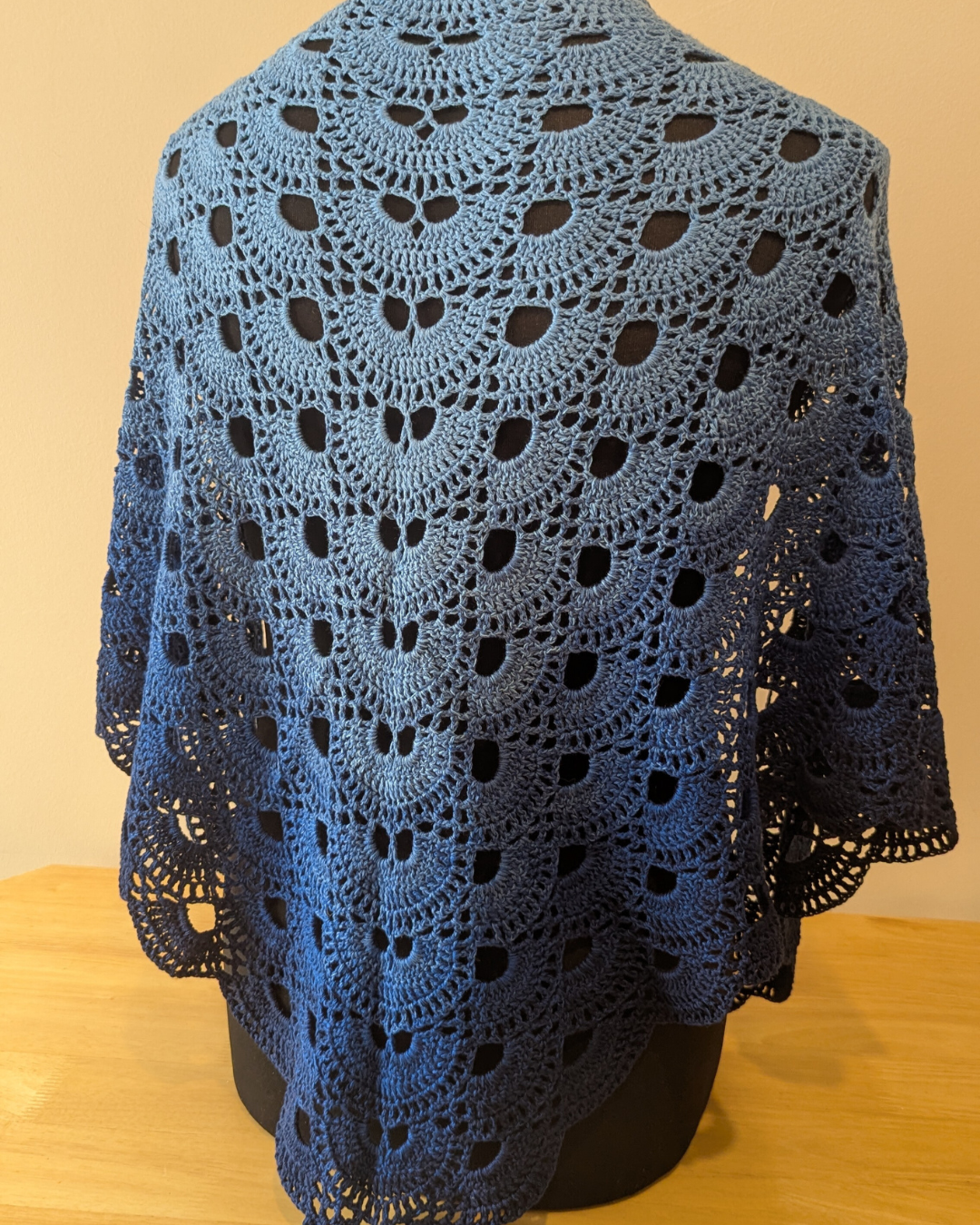 Blue crochet shawl on a wooden surface with a beige background
