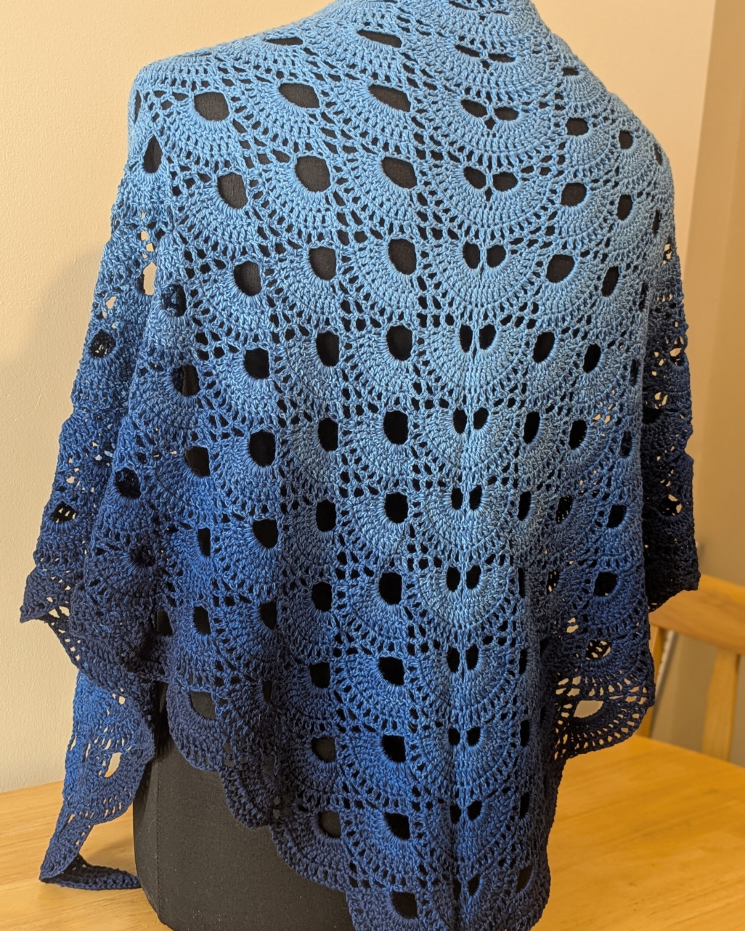 Blue crocheted shawl on a mannequin against a beige wall.