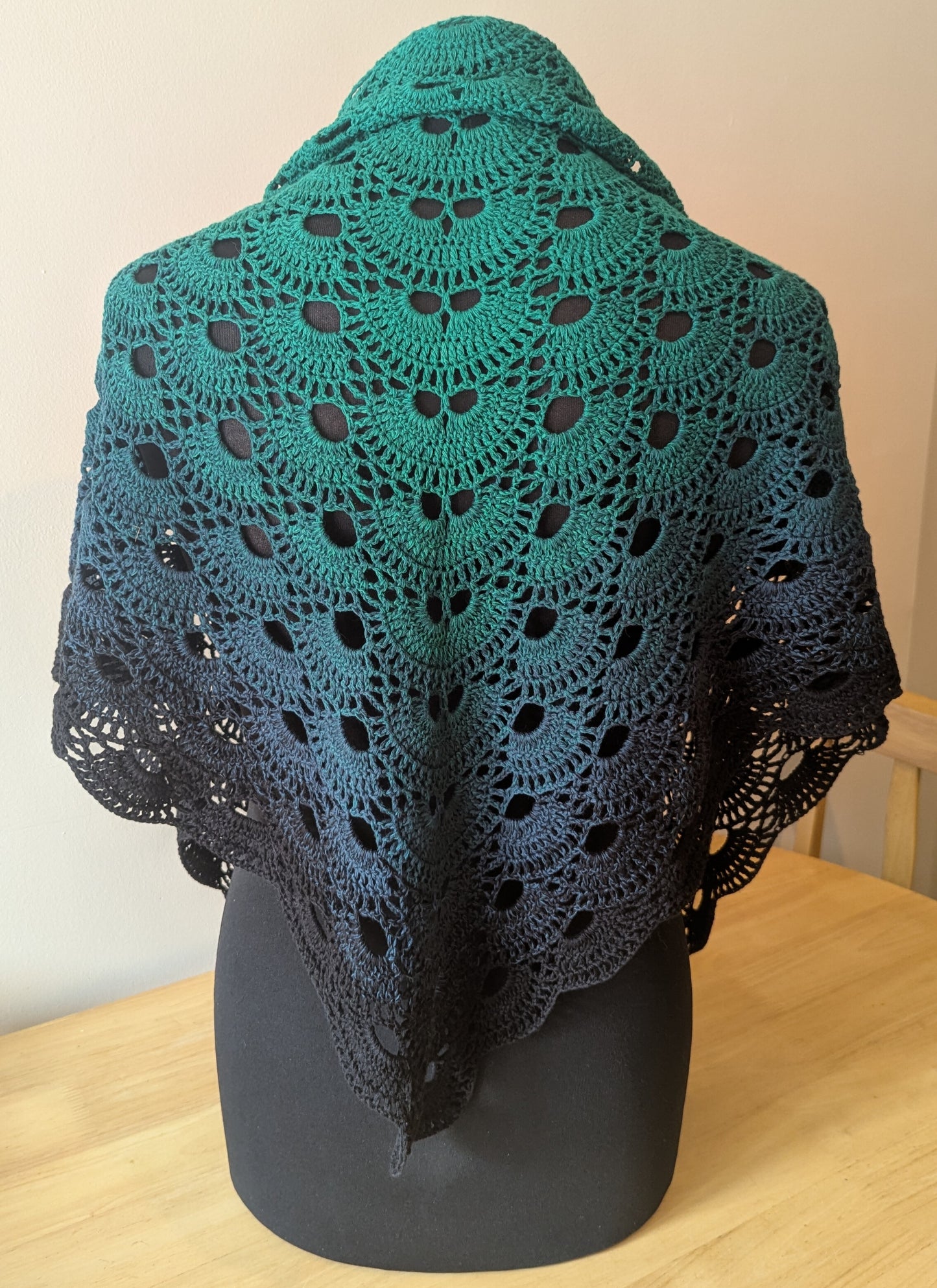 Green and black crocheted shawl on a mannequin against a plain background