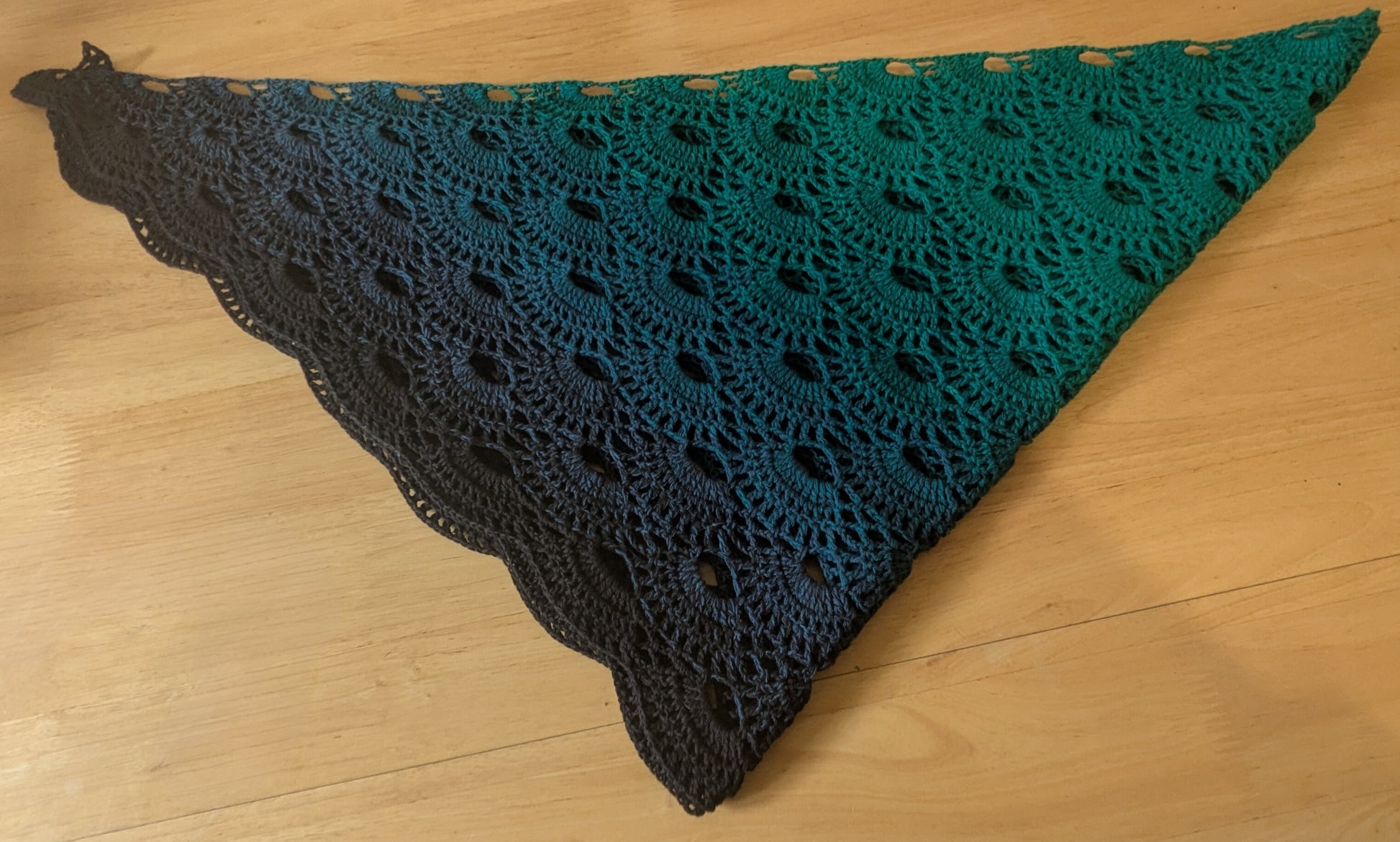Folded up crocheted shawl with green and black pattern on a wooden surface