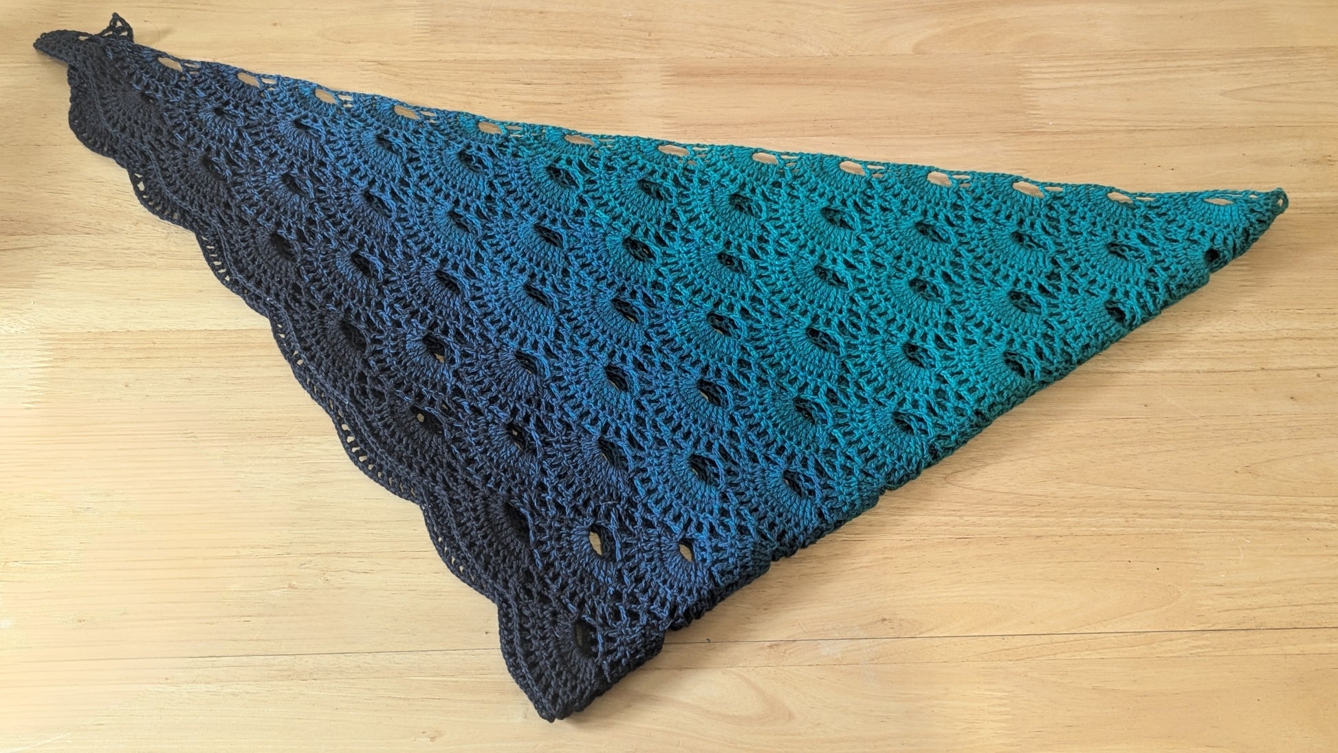 Crocheted shawl with a gradient of blue and black on a wooden surface