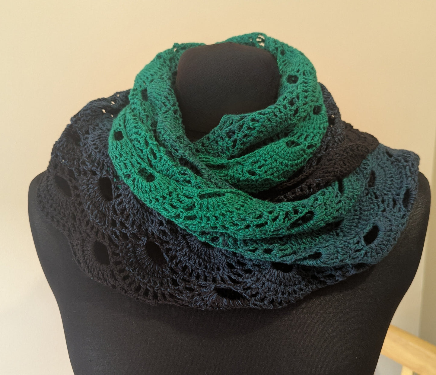 Green crocheted shawl on a mannequin against a beige background.