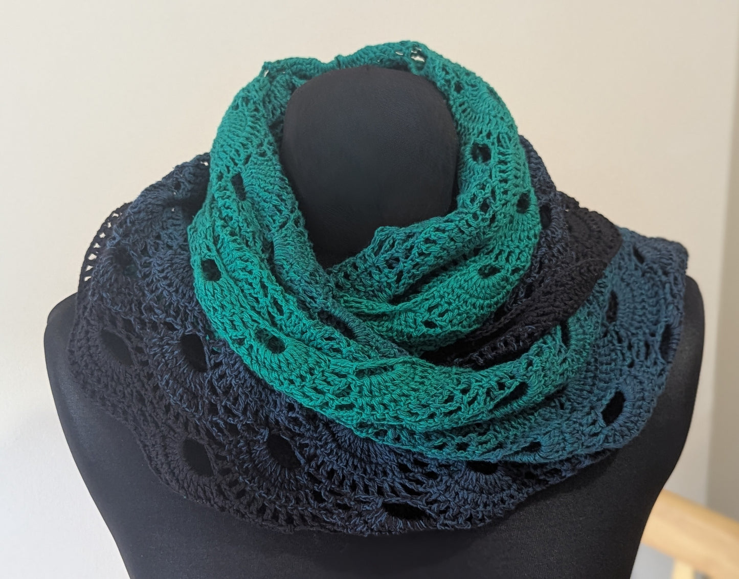 Green and black blue crocheted shawl on a mannequin against a white background