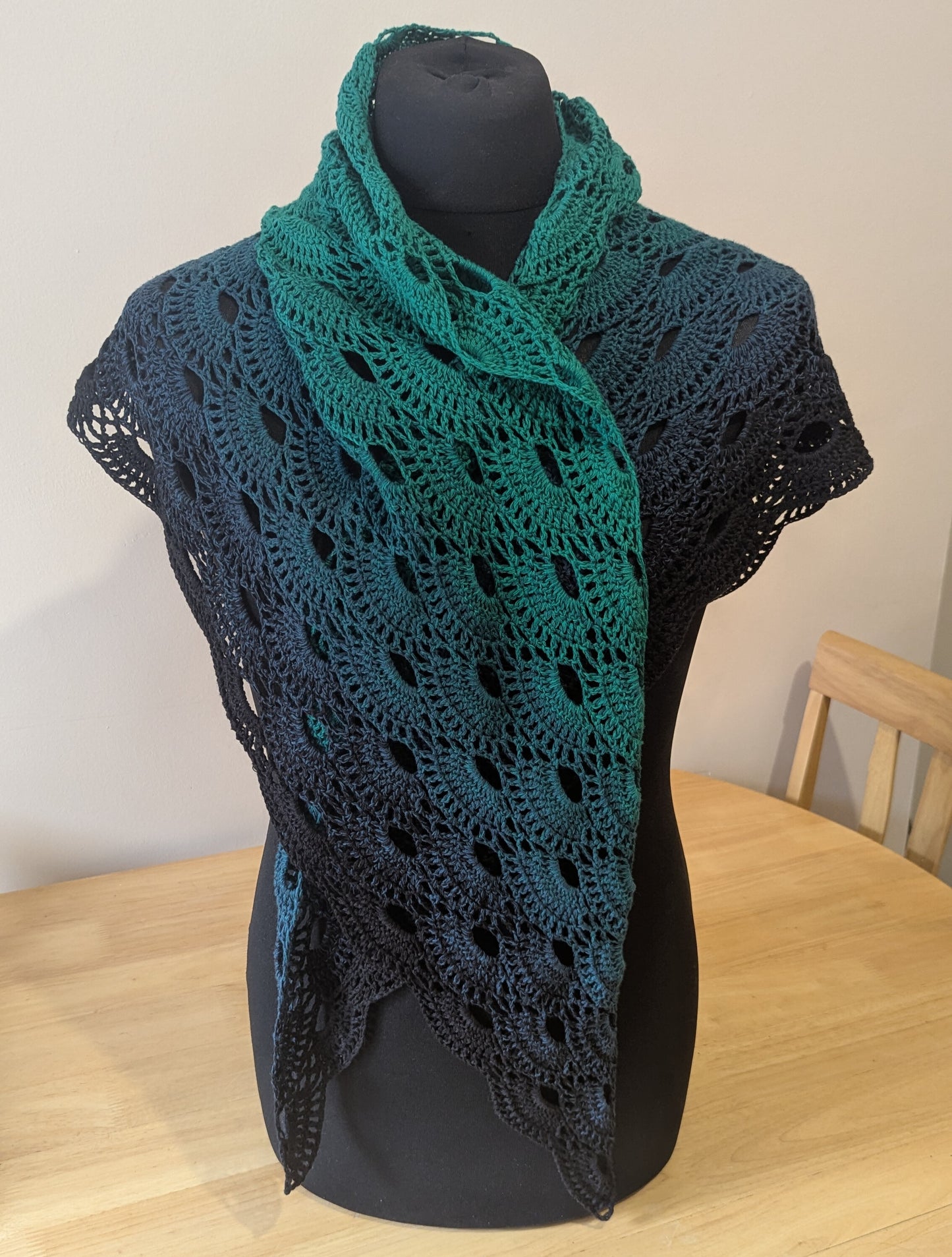 Crochet shawl in green and black on a black mannequin against a plain background