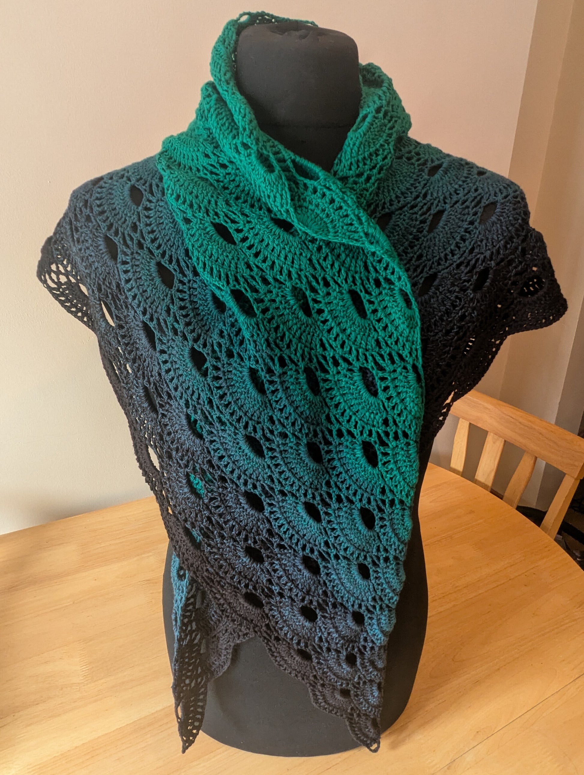 Green and black crocheted shawl on a mannequin against a neutral background