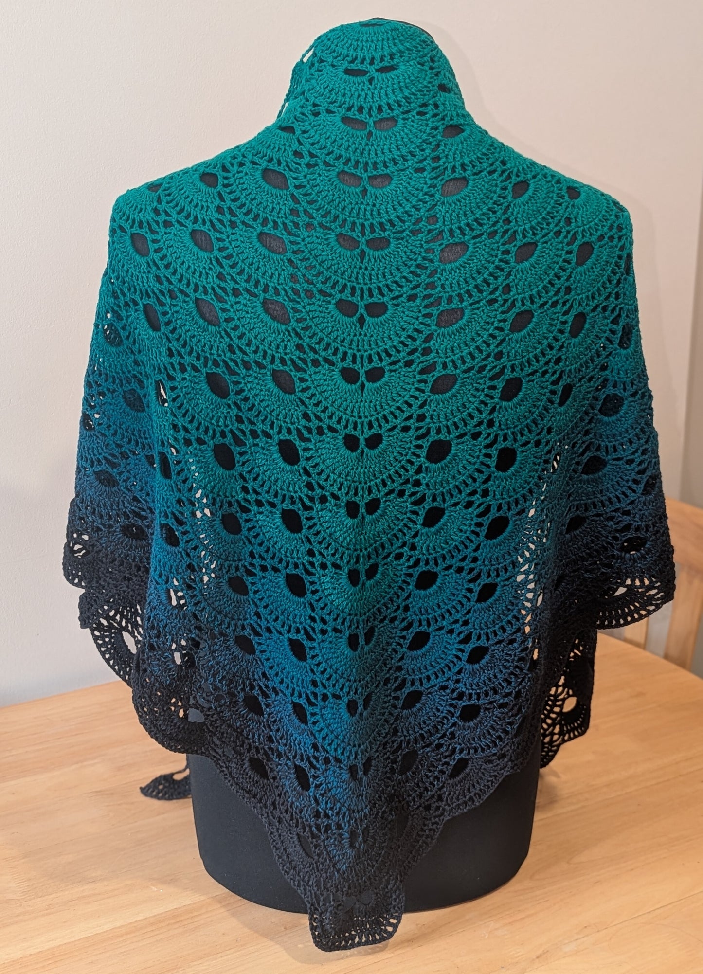 Green and black crocheted shawl on a mannequin against a plain background