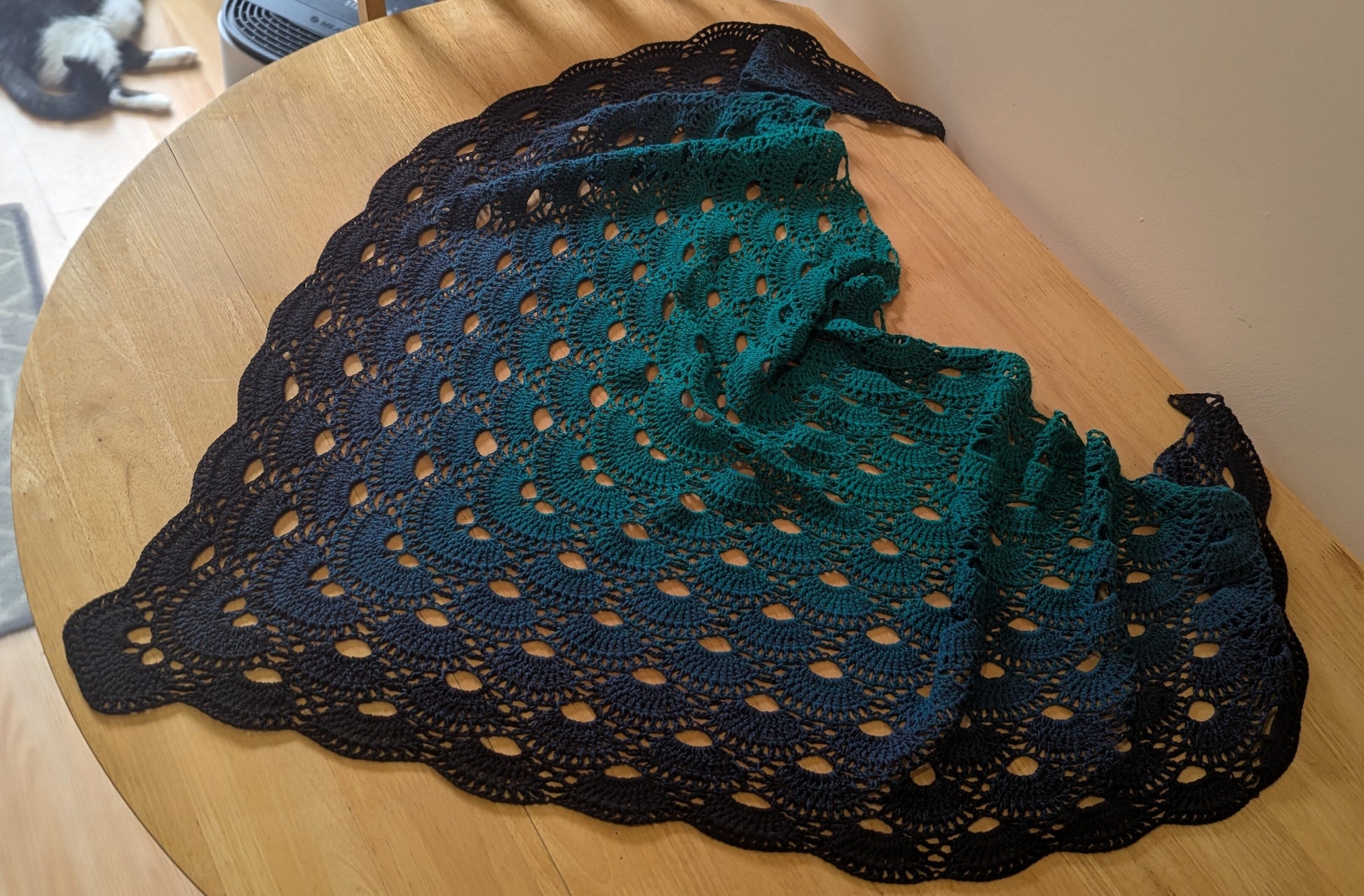 Crocheted shawl with a black border on a wooden surface