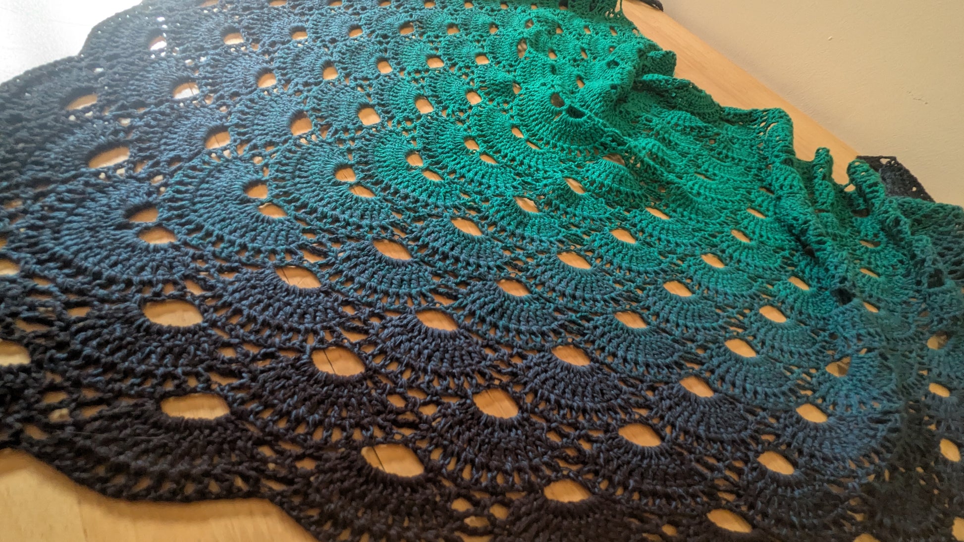 Close-up of a crocheted shawl with a scalloped edge on a wooden surface.